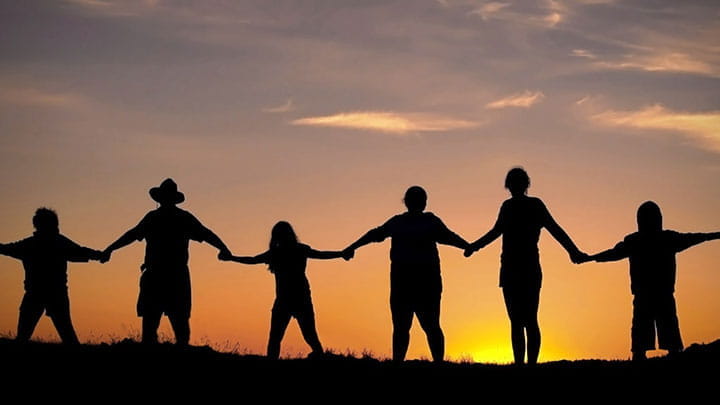Six humans holding hands in front of sunset 