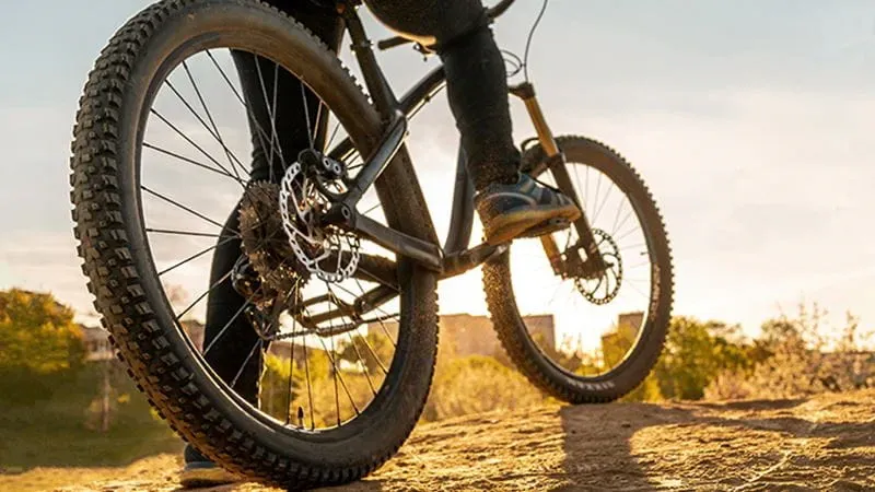 Bicycle wheels of mountain bike close up image on sunset, persons foot on one pedal