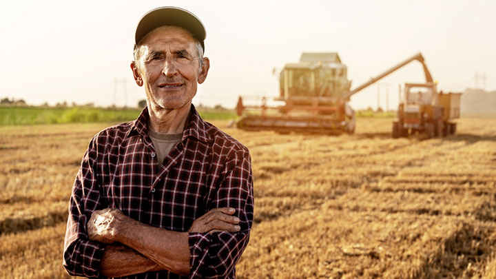 Satisfied farmer standing on fertile field harvested by tractor