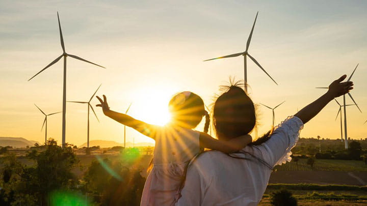 Adult and child overlooking wind turbines at sunset, representing renewable energy and climate action.