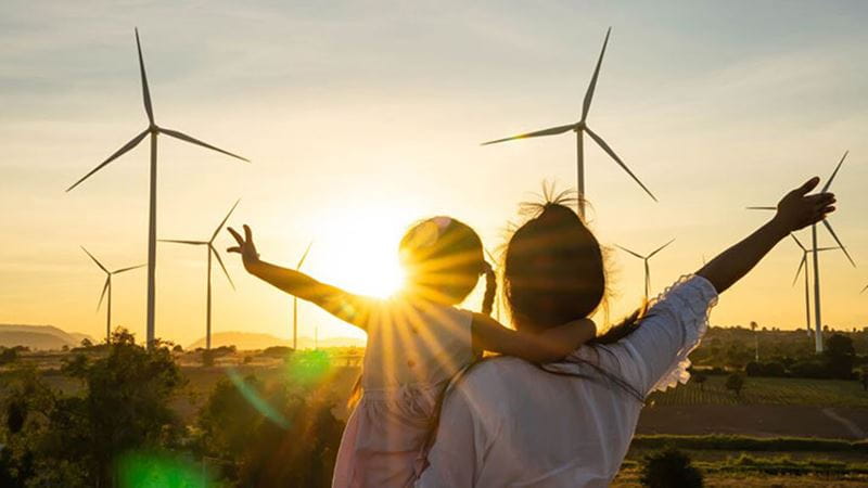 Adult and child overlooking wind turbines at sunset, representing renewable energy and climate action.