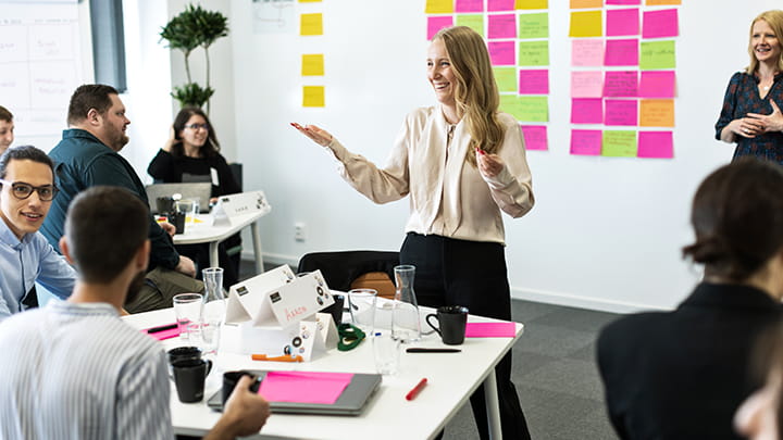 Facilitator leading an interactive workshop at Trelleborg Group University, with participants seated at tables discussing ideas and colorful notes on the wall behind them.