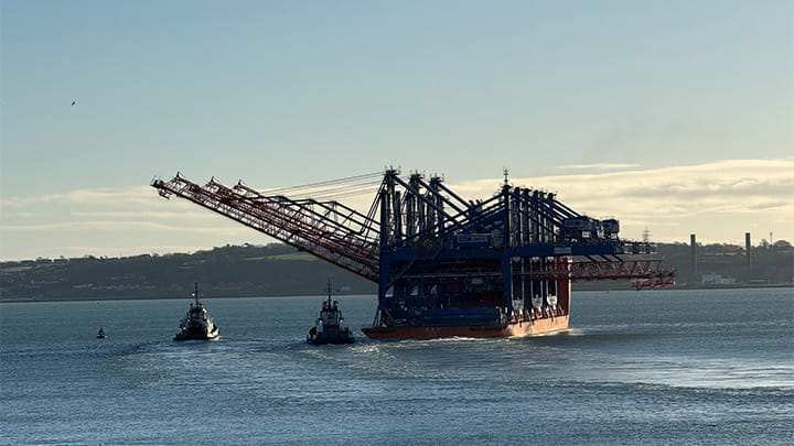 Tugboats assist a large heavy-lift vessel carrying ship-to-shore container cranes through Cork harbour