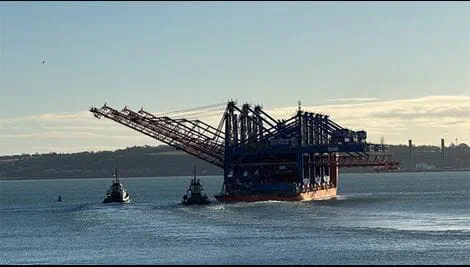 Tugboats assist a large heavy-lift vessel carrying ship-to-shore container cranes through Cork harbour