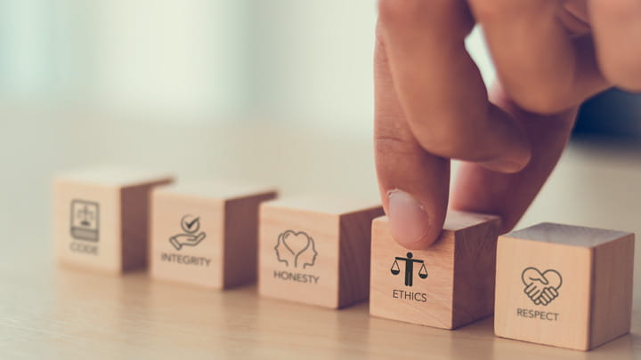 Hand arranging wooden blocks labeled Code, Integrity, Honesty, Ethics, and Respect on a table
