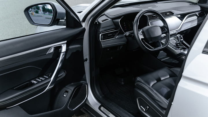 Intérieur de voiture avec porte conducteur ouverte, volant, tableau de bord et siège avant.