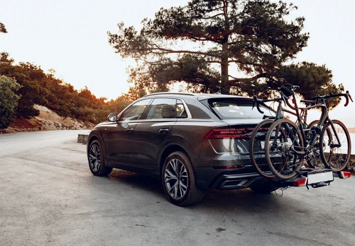 SUV oscuro estacionado en una carretera panorámica al atardecer con dos bicicletas montadas en un portabicicletas trasero