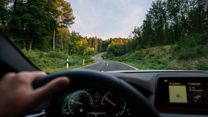 Driver’s view of a winding road through a green forest from inside a car