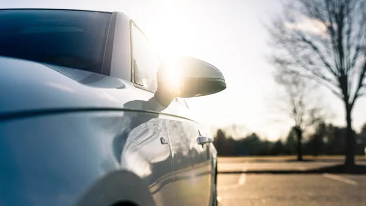 Silver car parked outdoors with sunlight reflecting off its side mirror and body