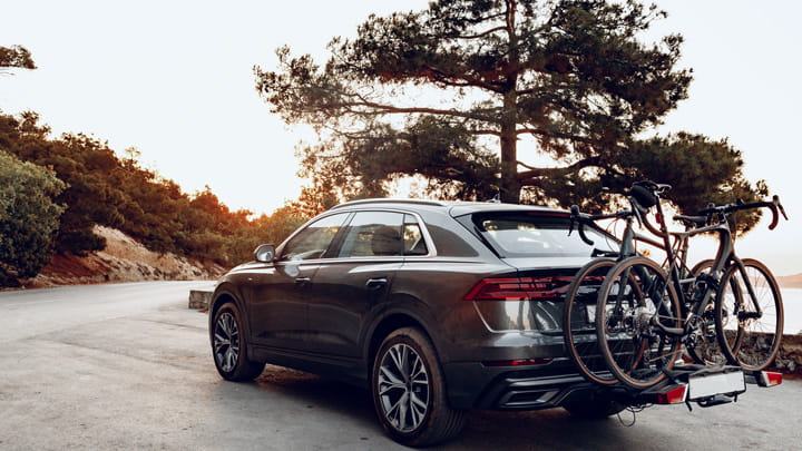 SUV sombre garé sur une route panoramique au coucher du soleil avec deux vélos fixés sur un porte-vélos arrière