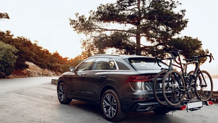 Dark SUV parked on a scenic road at sunset with two bicycles mounted on a rear bike rack