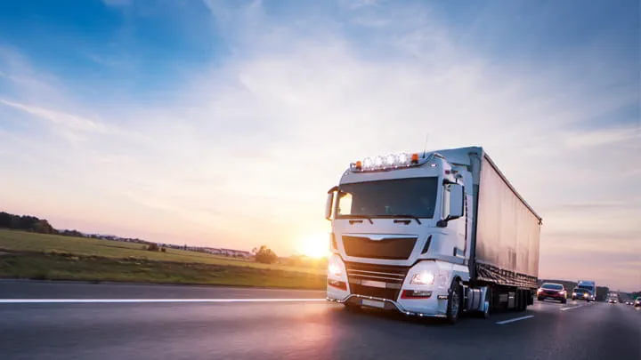 White cargo truck driving on a highway at sunset with a clear sky in the background