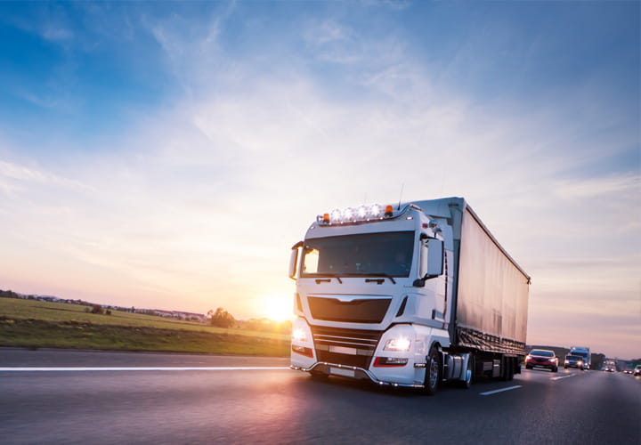 Camion blanc roulant sur une autoroute au coucher du soleil, avec un ciel dégagé en arrière-plan