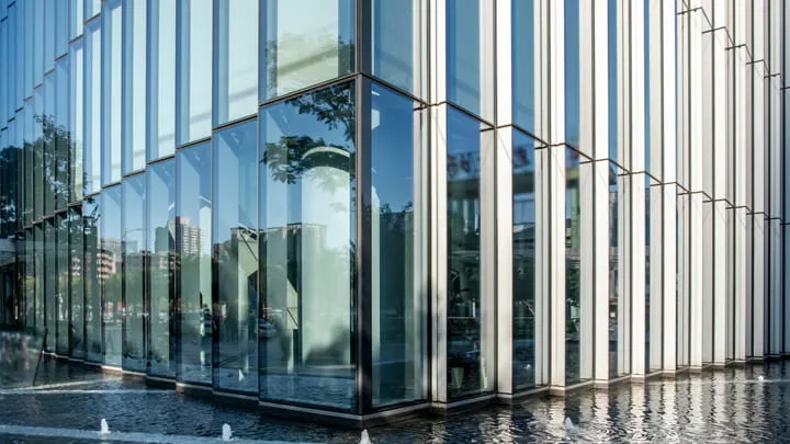 Modern glass curtain wall facade with reflective panels on a high-rise building under a clear blue sky