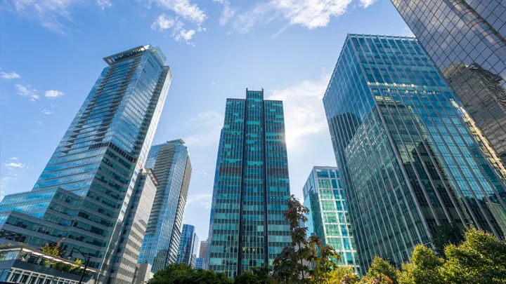 Cluster of modern glass skyscrapers under a blue sky, showcasing sleek facades and reflective surfaces