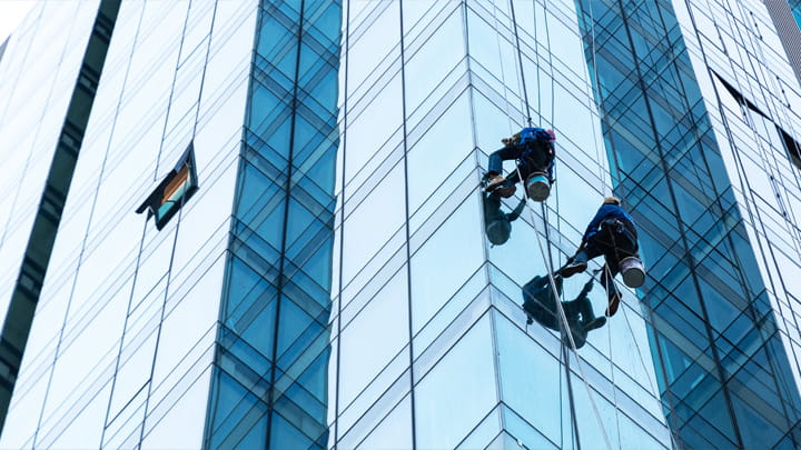 Two workers suspended on ropes cleaning or restoring glass panels on a tall modern building facade