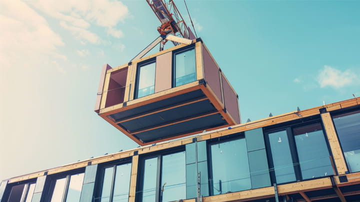 Edificio modular personalizable: Grúa ensamblando módulos prefabricados, permitiendo diseños y soluciones de sellado específicos para cada proyecto.