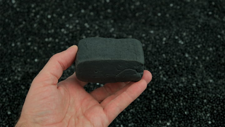 Hand holding a black rubber compound sample in front of rubber granules, highlighting raw material quality and formulation expertise