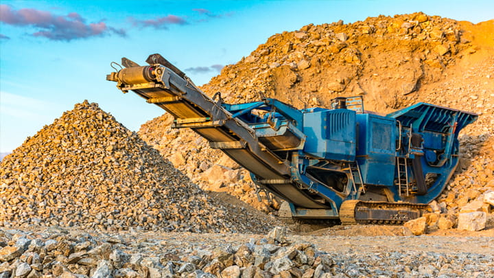Mobile crushing machine processing stone in a quarry with gravel piles and rocky terrain