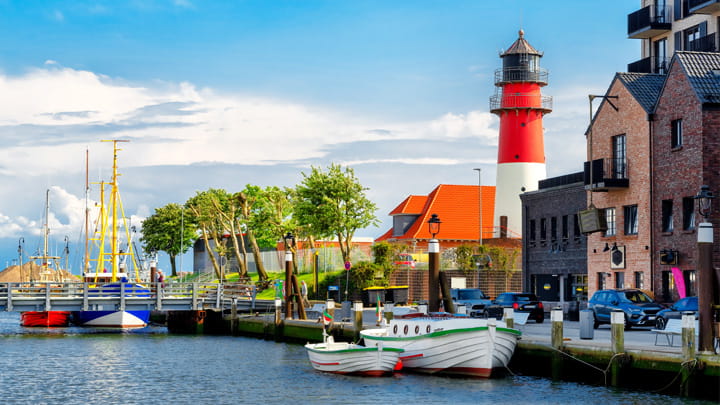 Fishing boats moored in a harbor near a red and white lighthouse and waterfront buildings.
