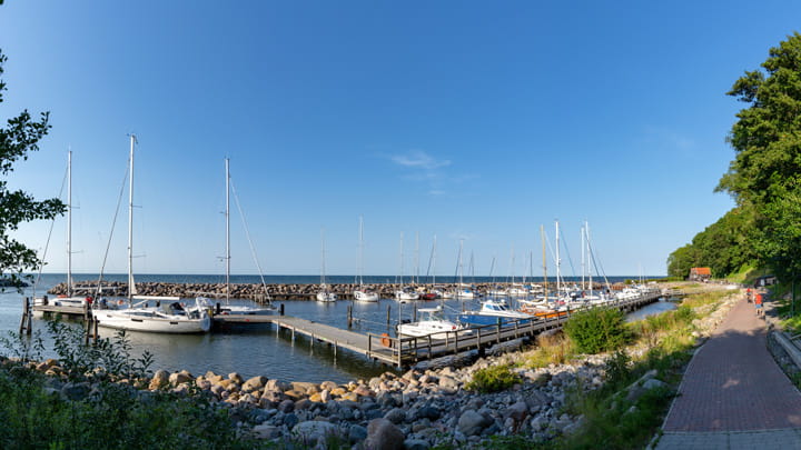 Two people walking along a marina dock with boats and yachts at sunset, carrying bags