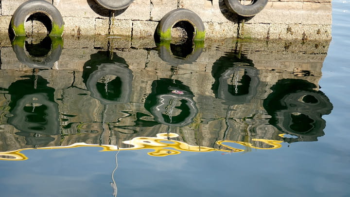 Black marine fenders mounted along a dock, protecting the quay beside calm water and waterfront buildings