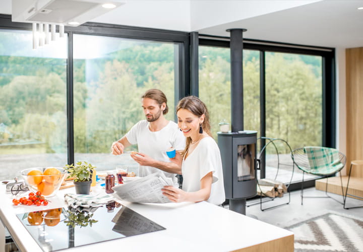 Zwei Personen bereiten gemeinsam Essen in einer modernen Küche mit großen Fenstern und Blick auf eine grüne Landschaft zu