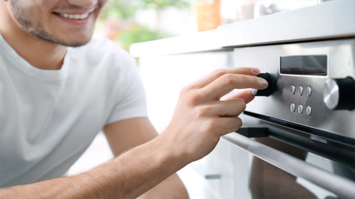 Person adjusting the temperature knob on a modern stainless-steel oven in a kitchen