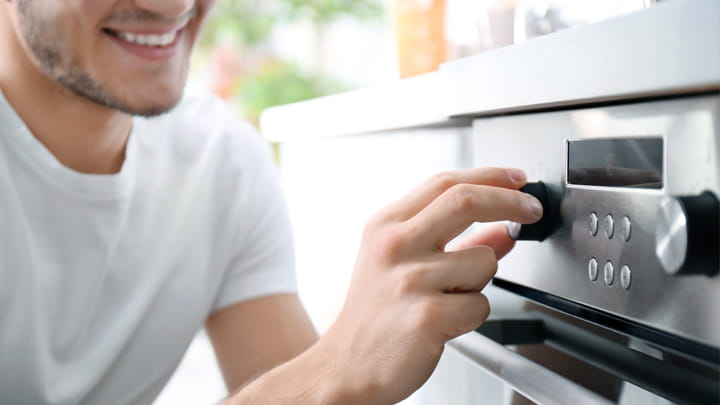 Person adjusting the temperature knob on a modern stainless-steel oven in a kitchen