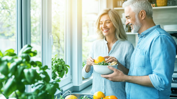 Una pareja en una cocina moderna, sosteniendo un plato de comida sana y colorida