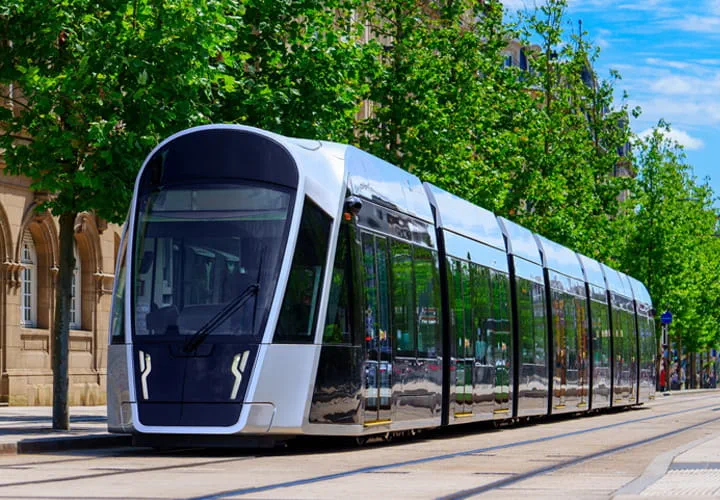 Tramway électrique moderne circulant dans une rue urbaine bordée d’arbres, illustrant une mobilité durable en ville.