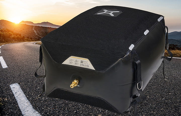 Lyra lifting bag with straps and a side valve placed on a winding mountain road at sunset.