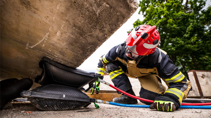 A firefighter kneels on the ground, using a lifting bag to raise a large boulder