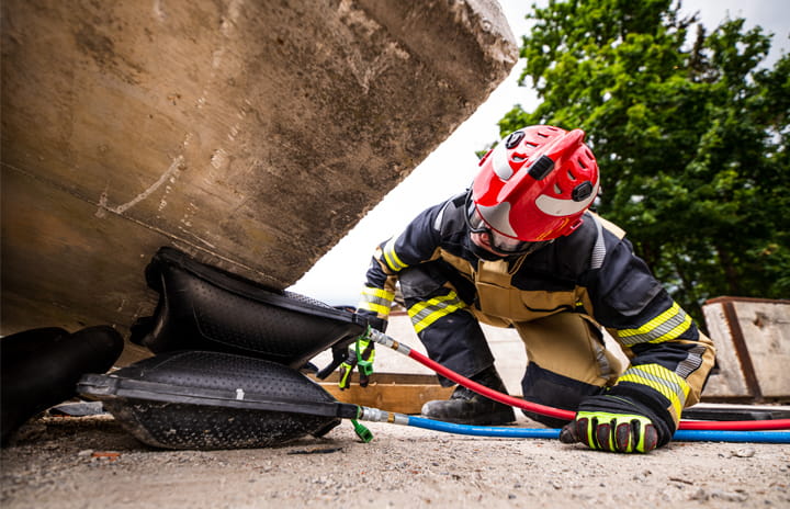 A firefighter kneels on the ground, using a lifting bag to raise a large boulder