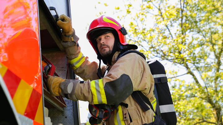 A firefighter, fully equipped with safety gear, standing next to a fire truck