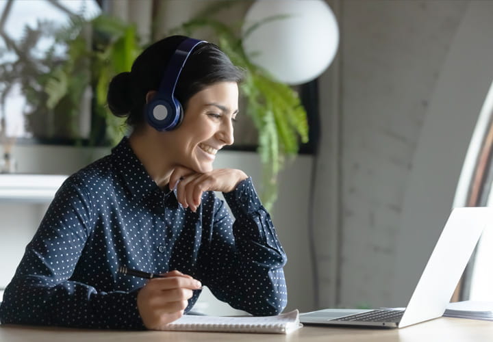 Person wearing headphones working at a desk with a laptop and notebook
