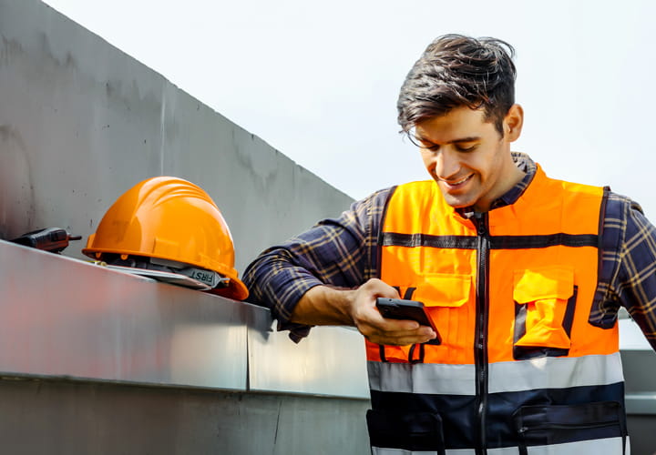young worker looking on his mobile phone with a safety vest