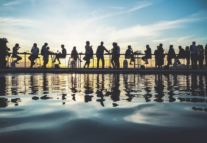 News and events banner with people sitting in sunset with water