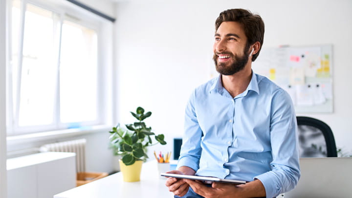 About us Smiling businessman with headphones using a digital tablet in his office